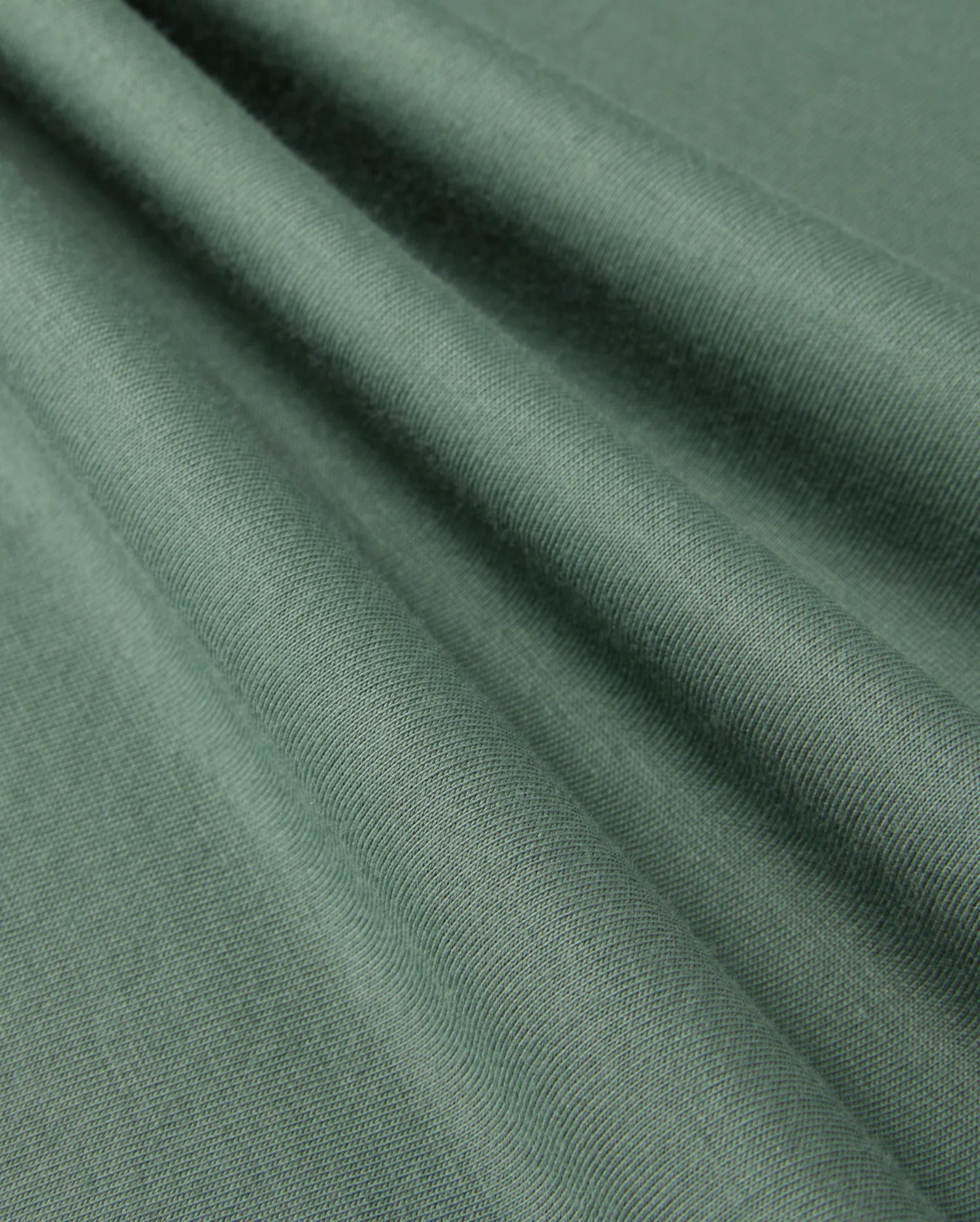 A close-up of folded Pima cotton fabric from the KIDS ALBERTON LONG SLEEVE TEE by Psycho Bunny, showcasing its smooth texture and subtle sheen. The fabric is draped in soft, diagonal folds, highlighting the material's flexibility and fine weave—perfect for creating a luxurious layering piece or a cozy long sleeve tee.