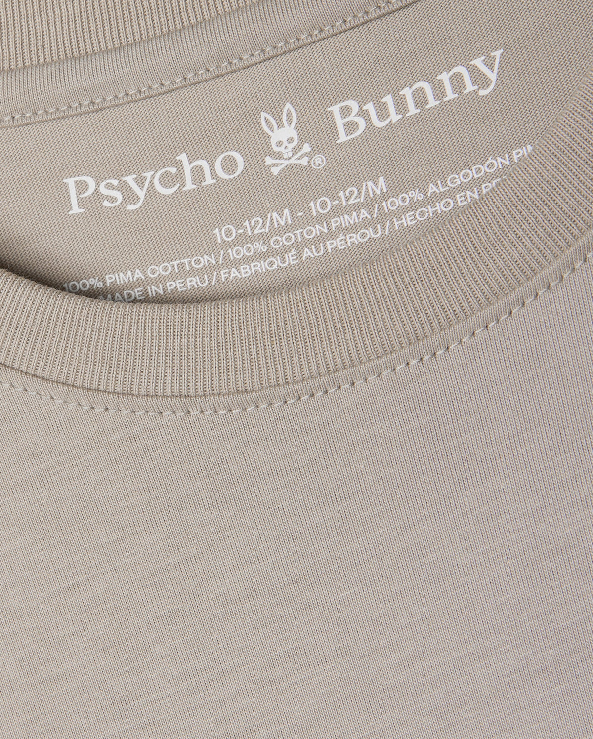 Close-up of a beige KIDS ALBERTON LONG SLEEVE TEE - B0T867D200 by Psycho Bunny, highlighting the brand logo and size details (10-12/M) inside the neckline. This regular fit tee is made from 100% Pima cotton for exceptional softness and quality, crafted in Peru.