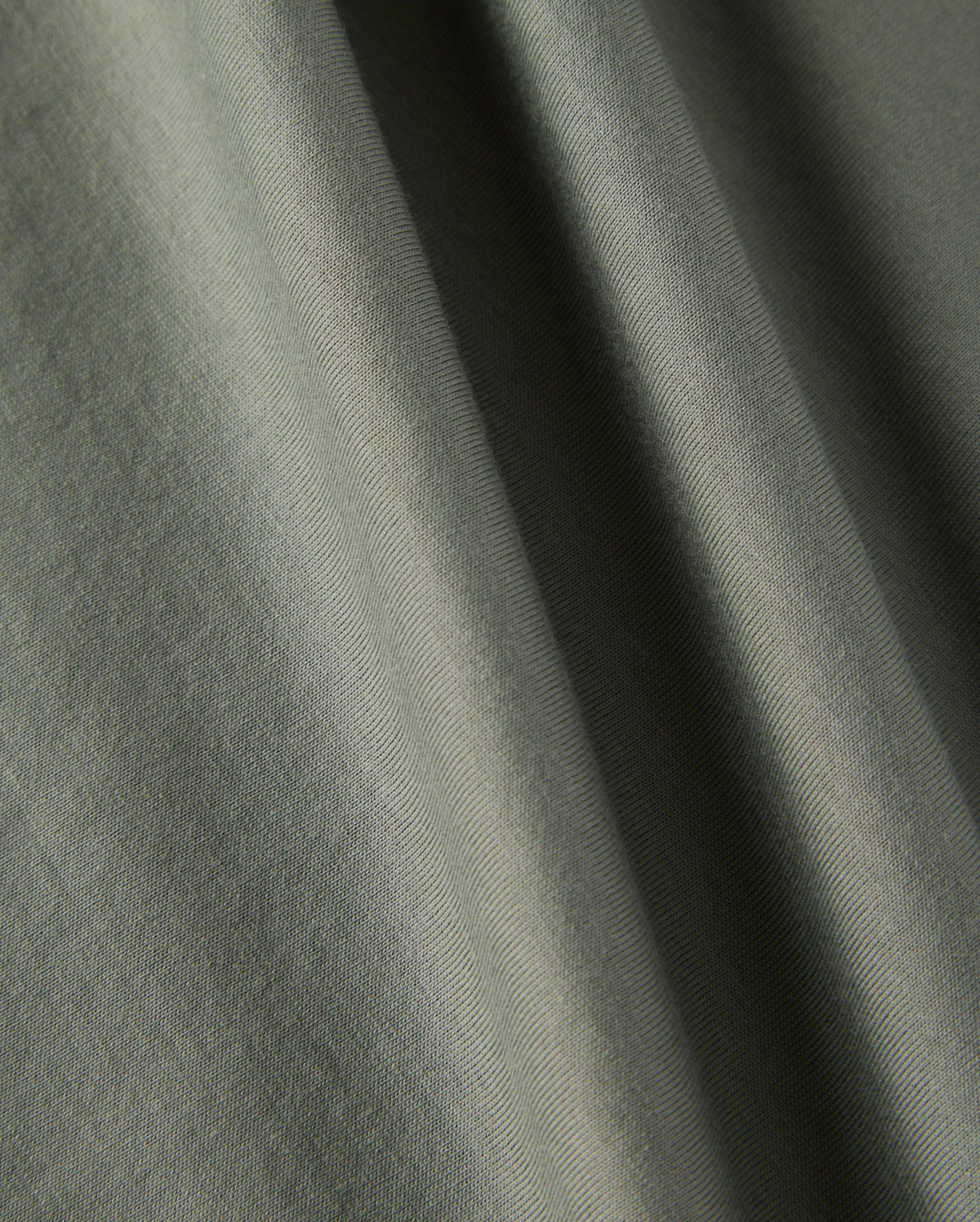Close-up image of a green fabric showcasing its soft texture and weaving pattern. Made from 100% Pima cotton, the material is perfect for Psycho Bunny's Kids Classic Crew Neck Tee (B0U014B200). Light and shadows create subtle variations in the fabric's color.