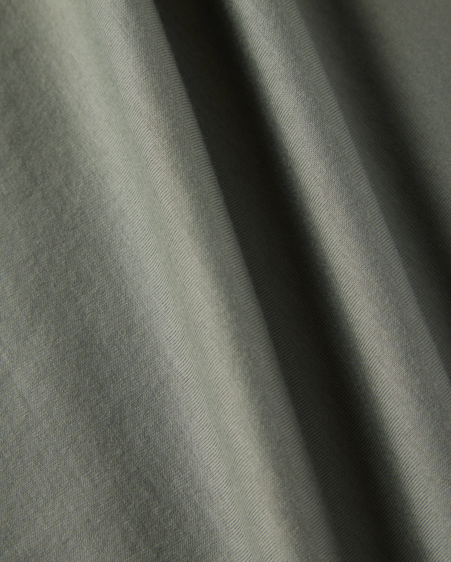 Close-up image of a green fabric showcasing its soft texture and weaving pattern. Made from 100% Pima cotton, the material is perfect for Psycho Bunny's Kids Classic Crew Neck Tee (B0U014B200). Light and shadows create subtle variations in the fabric's color.