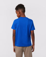 A child with short hair is seen from behind, sporting a vibrant blue KIDS CLASSIC CREW NECK TEE by Psycho Bunny and beige pants against a plain light background.