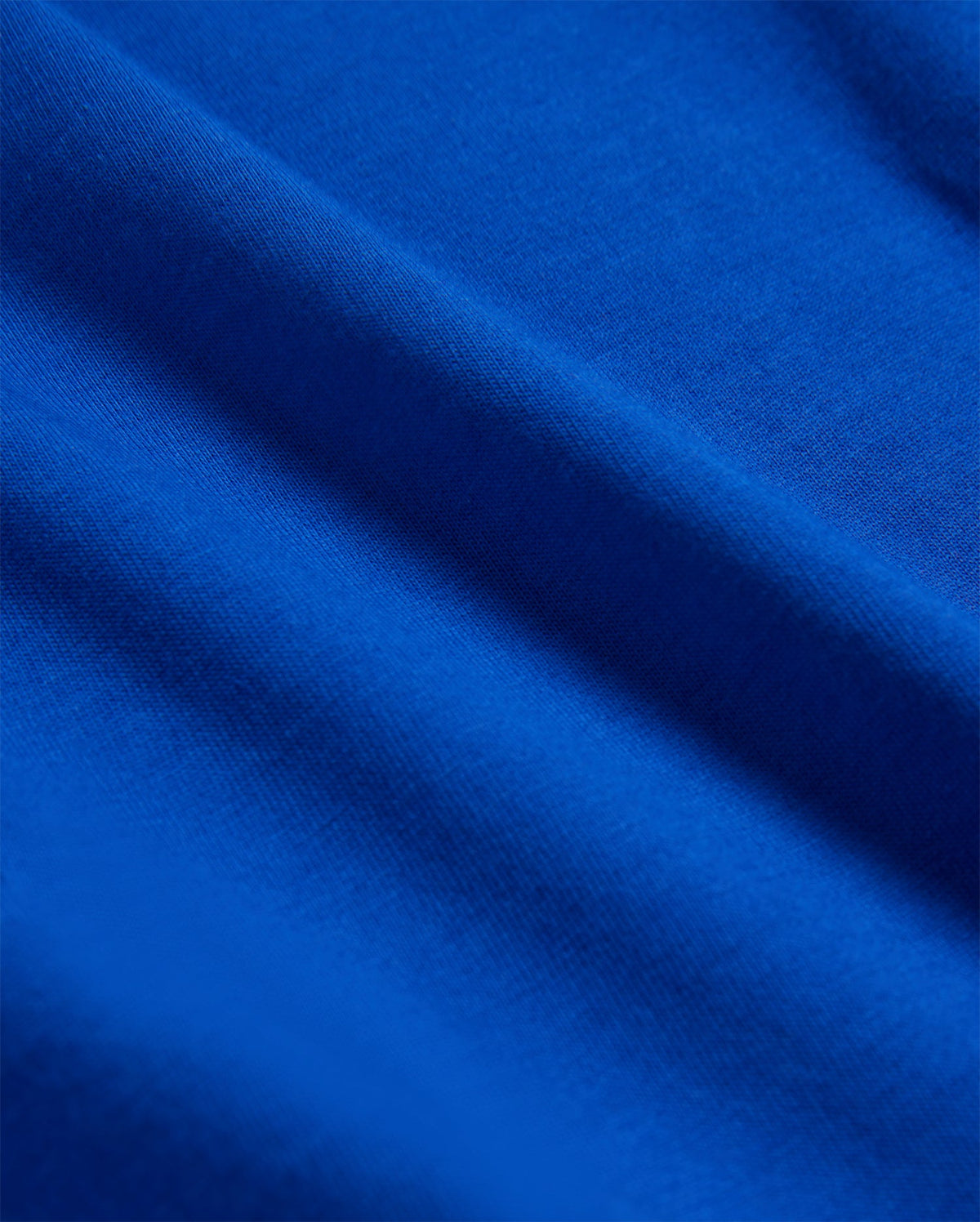 Close-up of a blue fabric with visible texture and gentle folds, creating a sense of depth and softness. Made from luxurious Pima cotton, the lighting highlights the rich color and smooth surface of the KIDS CLASSIC CREW NECK TEE - B0U014CRPC by Psycho Bunny.