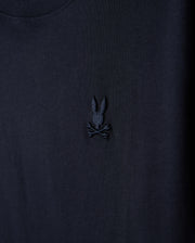 A close-up of the Kids Embroidered Classic Tee by Psycho Bunny, showcasing a dark-colored fabric with a black embroidered design featuring a bunny head with long ears above crossed bones, akin to a skull and crossbones, crafted from luxurious Peruvian Pima cotton.
