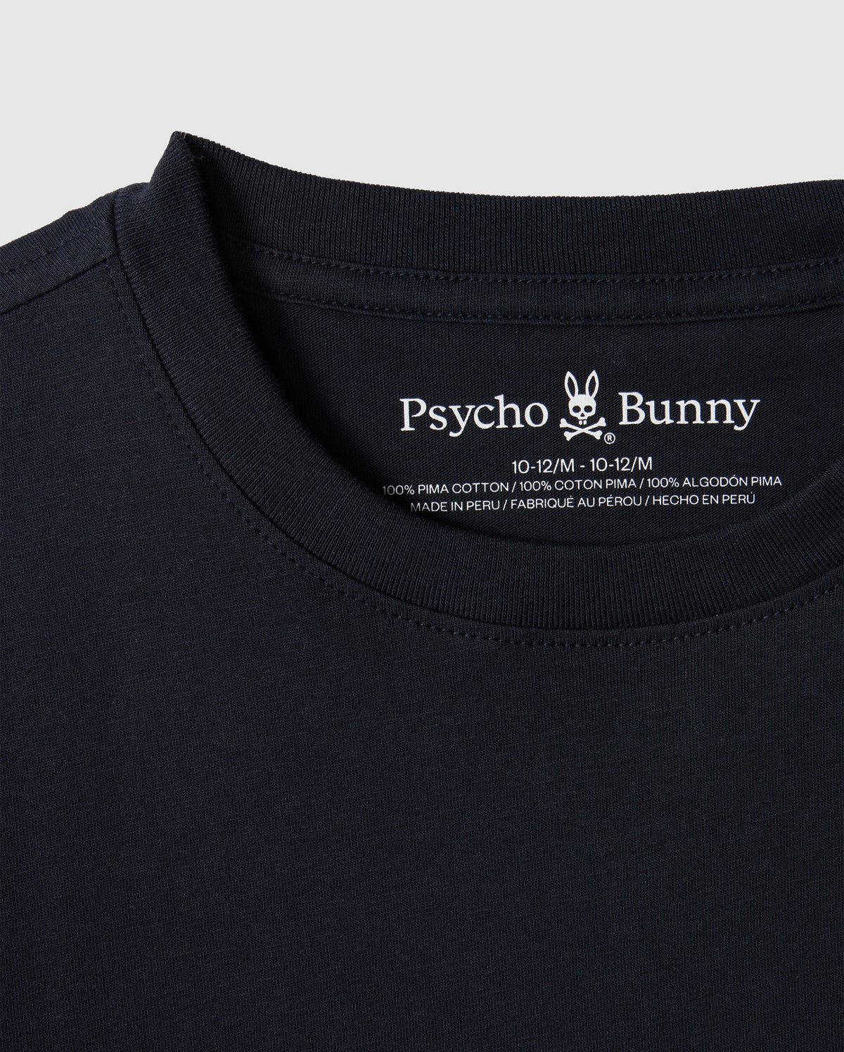Close-up of the KIDS EMBROIDERED CLASSIC TEE - B0U020AR00 in black, featuring the Psycho Bunny brand logo and text on the inside neck area. It boasts an embroidered chest bunny, and the label confirms it's made of 100% Peruvian Pima cotton, manufactured in Peru.