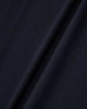 Close-up image of a dark navy blue fabric with a diagonal fold running from the bottom left to the top right. The texture, reminiscent of Peruvian Pima cotton, appears smooth and slightly matte, with subtle variations in color due to the lighting and fabric draping. The fabric is from Psycho Bunny's KIDS EMBROIDERED CLASSIC TEE - B0U020AR00.