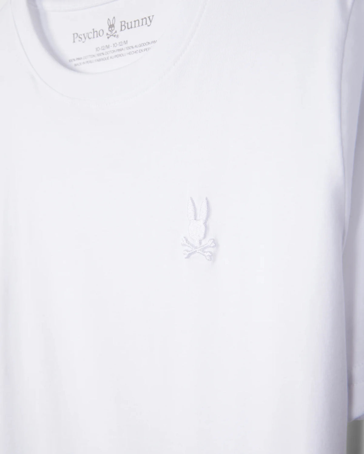 The KIDS EMBROIDERED CLASSIC TEE - B0U020AR00 from Psycho Bunny is a premium white t-shirt crafted from Peruvian Pima cotton, featuring the brand's intricate embroidered chest Bunny logo with detailed bunny and crossed bones below.