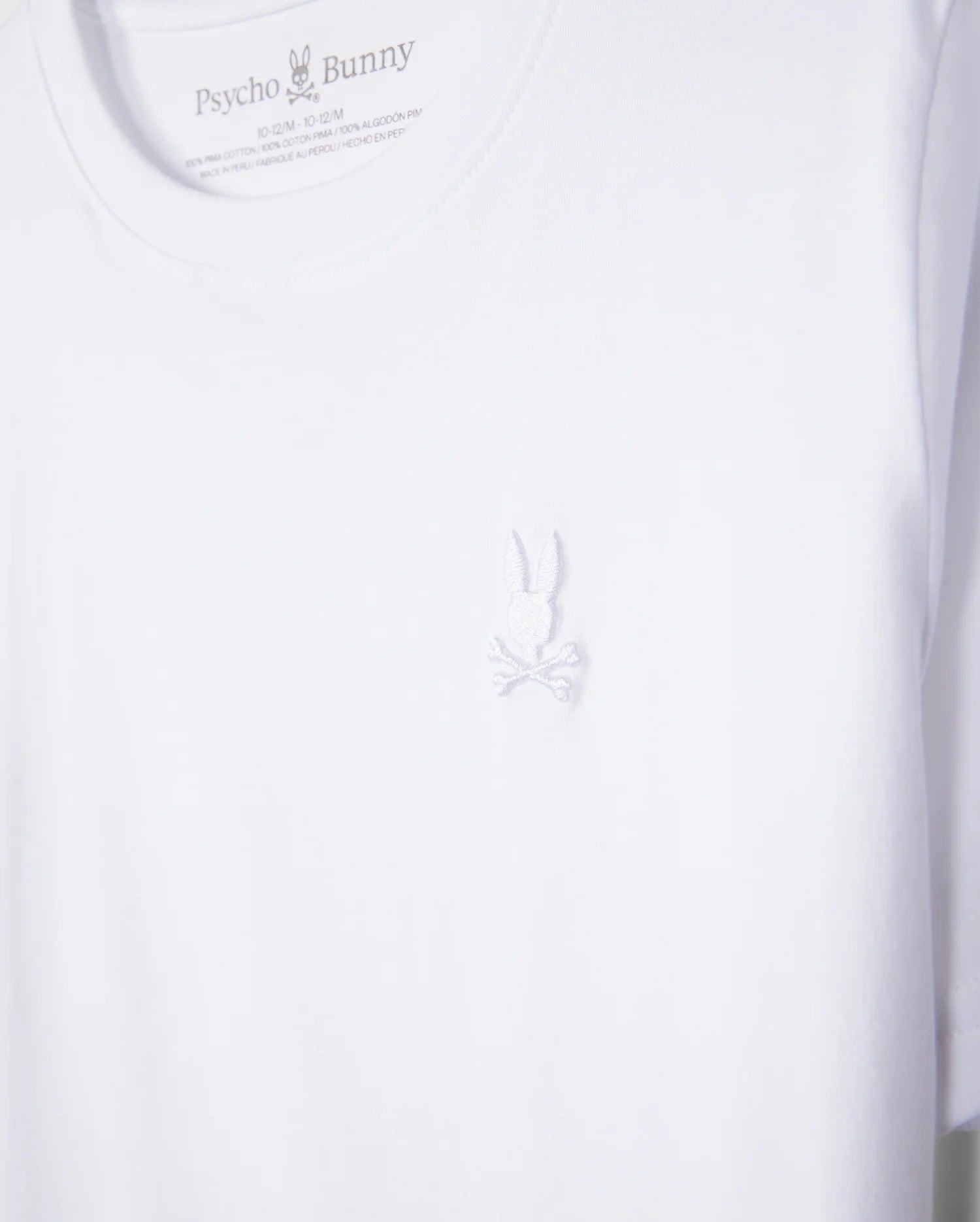 The KIDS EMBROIDERED CLASSIC TEE - B0U020AR00 from Psycho Bunny is a premium white t-shirt crafted from Peruvian Pima cotton, featuring the brand's intricate embroidered chest Bunny logo with detailed bunny and crossed bones below.