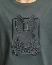 Dark green KIDS PIERCE GRAPHIC TEE by Psycho Bunny, crafted from Pima cotton, featuring a stylish embossed design with bunny embroidery that displays a rabbit silhouette above crossed bones.