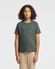 A young individual with curly hair sports a KIDS PIERCE EMBROIDERED GRAPHIC TEE by Psycho Bunny in dark green. Against a plain white background, they effortlessly complement this casual look with beige pants.