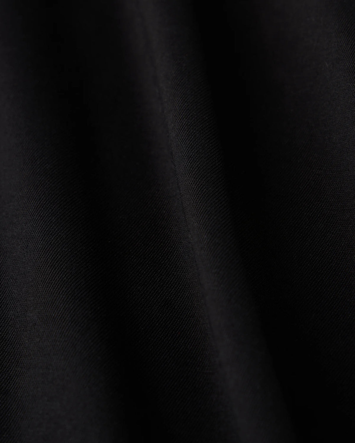 Close-up of a smooth black fabric crafted from luxurious Pima cotton on Psycho Bunny's KIDS HAWAII CITY TEE - B0U169Y1PC, featuring subtle diagonal lines and a soft sheen, evoking the sleek elegance reminiscent of volcanic island landscapes.