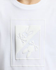 Close-up of the Psycho Bunny KIDS DOTSERO PRINTED GRAPHIC TEE - B0U197E200, a white children's shirt made from soft Peruvian Pima cotton. It features an eye-catching embossed puff print design that depicts a rabbit skull with crossbones and ears, split diagonally with one half upright and the other inverted.