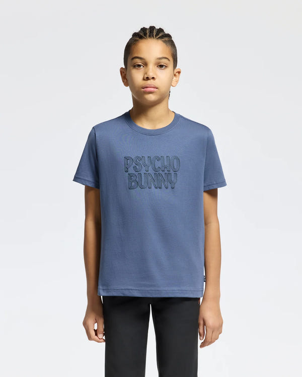 A young individual with braided hair is sporting the KIDS MONARC WORDMARK GRAPHIC TEE - B0U210E200 by Psycho Bunny, made from lightweight and durable Pima cotton, featuring the "PSYCHO BUNNY" text on the front. They stand confidently against a plain white background.