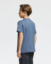 A young boy with short brown hair stands in a neutral pose, facing left. He is wearing a KIDS MONARC FRONT BUNNY GRAPHIC TEE - B0U211E200 by Psycho Bunny, along with black pants. The background is light gray, highlighting his classic look.