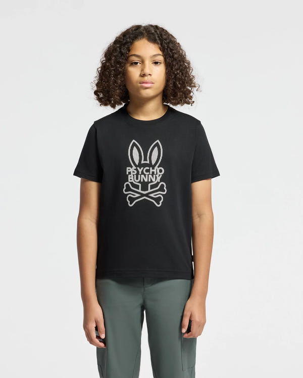A young person with curly hair sports the KIDS DUMON GRAPHIC TEE - B0U271E200 by Psycho Bunny, showcasing a trendy bunny and crossbones design. This black T-shirt, crafted from soft Pima cotton, is elegantly paired with their gray pants against a plain white backdrop.