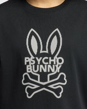 The KIDS DUMON GRAPHIC TEE - B0U271E200 by Psycho Bunny provides an up-close look at a black tee made from soft Pima cotton. It showcases a chic bunny logo with elongated ears above the words "PSYCHO BUNNY," accompanied by a crossed bones design underneath, seamlessly combining comfort with an edgy style.