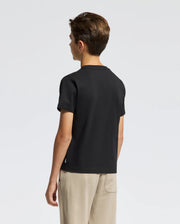A person with short hair is wearing a black KIDS DACANO FRONT GRAPHIC TEE by Psycho Bunny and beige pants, standing with their back to the camera against a plain white background.