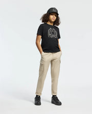 A person with curly hair is wearing a black cap, Psycho Bunny's Kids Melbourne Graphic Tee (B0U410F200) with a bunny graphic, beige cargo pants, and black sneakers while standing against a plain white background with hands in their pockets.
