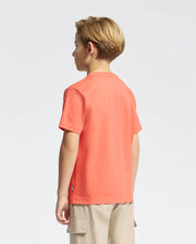 A young blonde child faces away, wearing an orange KIDS MELBOURNE GRAPHIC TEE by Psycho Bunny crafted from soft Peruvian Pima cotton, paired with beige cargo shorts, against a plain white backdrop.