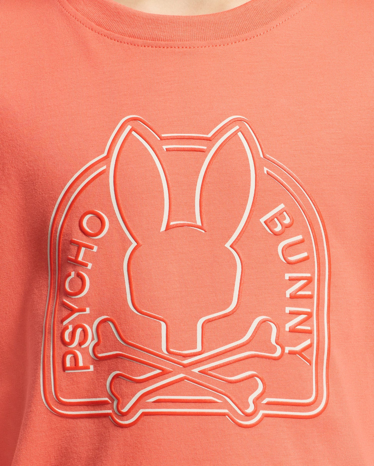 The KIDS MELBOURNE GRAPHIC TEE - B0U410F200 by Psycho Bunny features a bunny with elongated ears over crossbones, crafted from Peruvian Pima cotton. The words "Psycho Bunny" arch above this coral-colored t-shirt design.