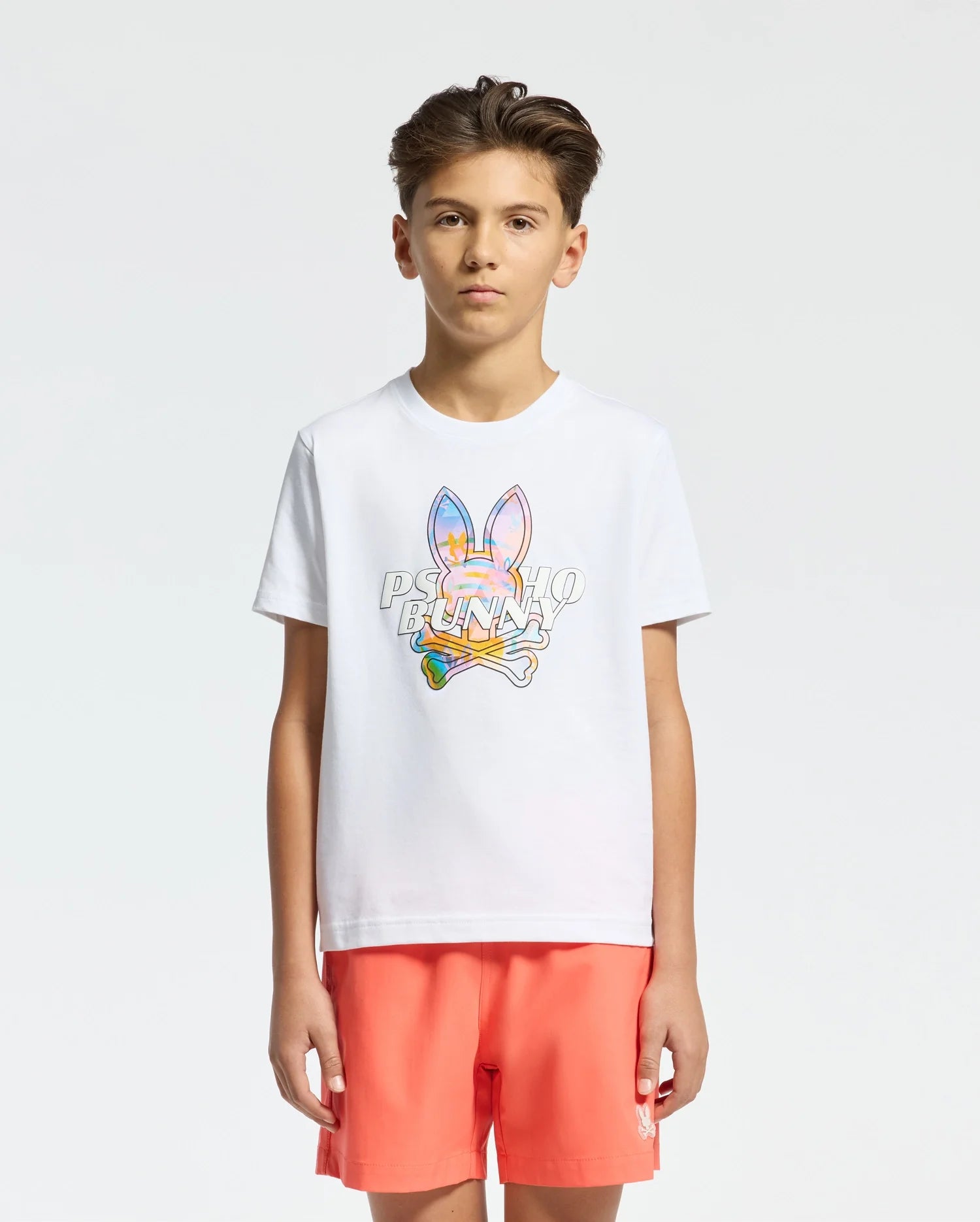 White jersey t-shirt with a large, vibrant multicolor Psycho Bunny skull graphic and text on the chest, paired with coral relaxed-fit shorts featuring a small white embroidered bunny logo.