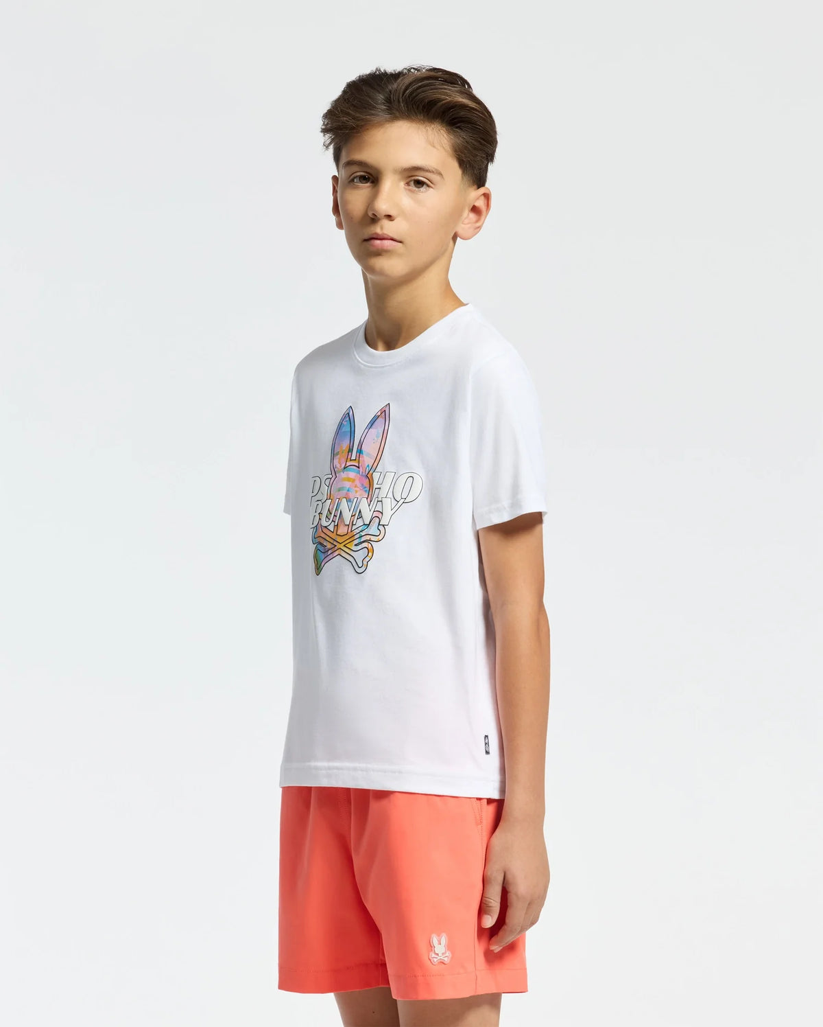 White jersey t-shirt with a large, vibrant Psycho Bunny skull and text graphic on the chest, paired with coral classic fit shorts featuring a small embroidered white bunny skull logo on the left leg.