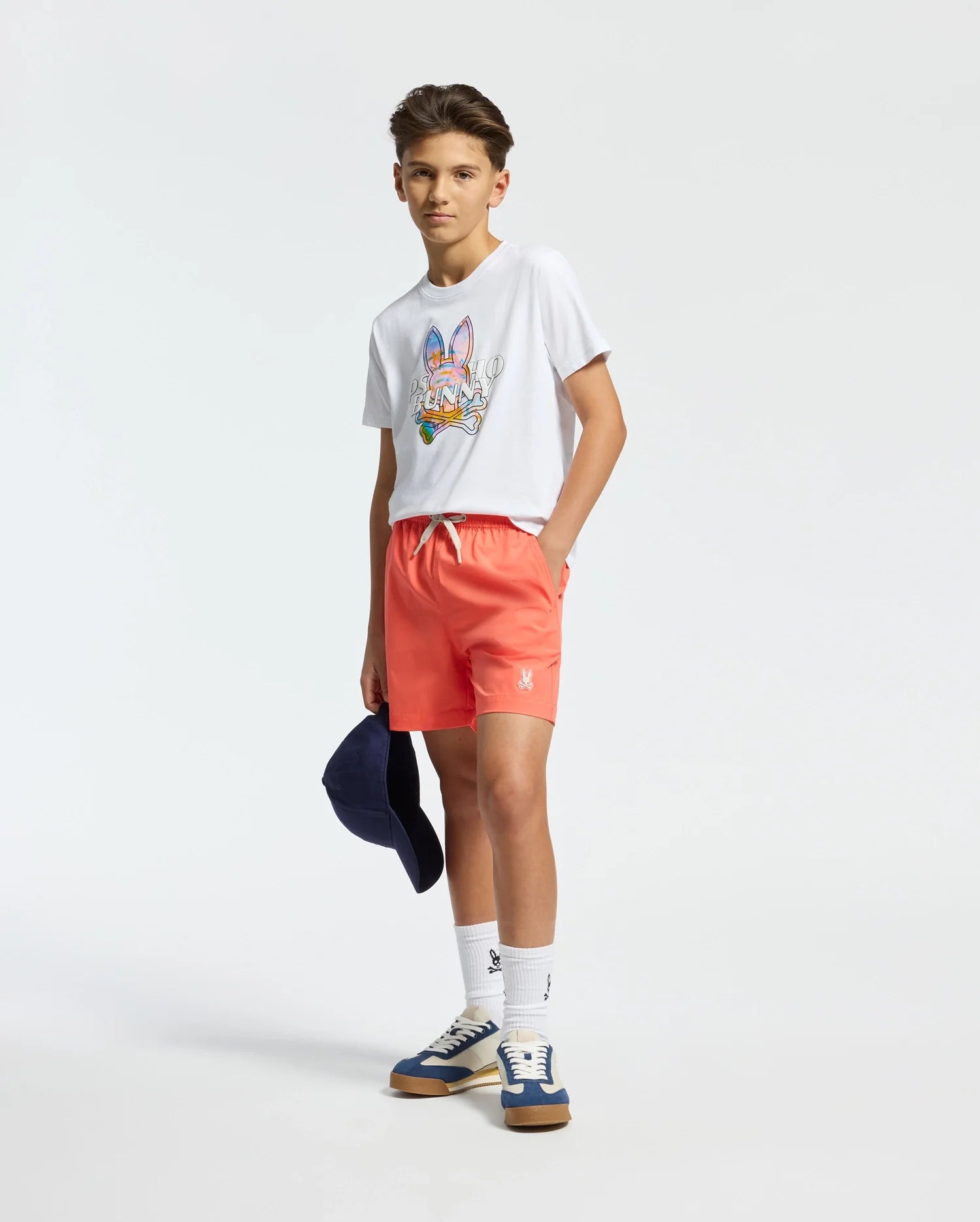 White jersey t-shirt with a large, multicolor Psycho Bunny skull graphic on the chest, paired with coral woven shorts featuring a white drawstring and a small embroidered bunny logo on the left thigh.