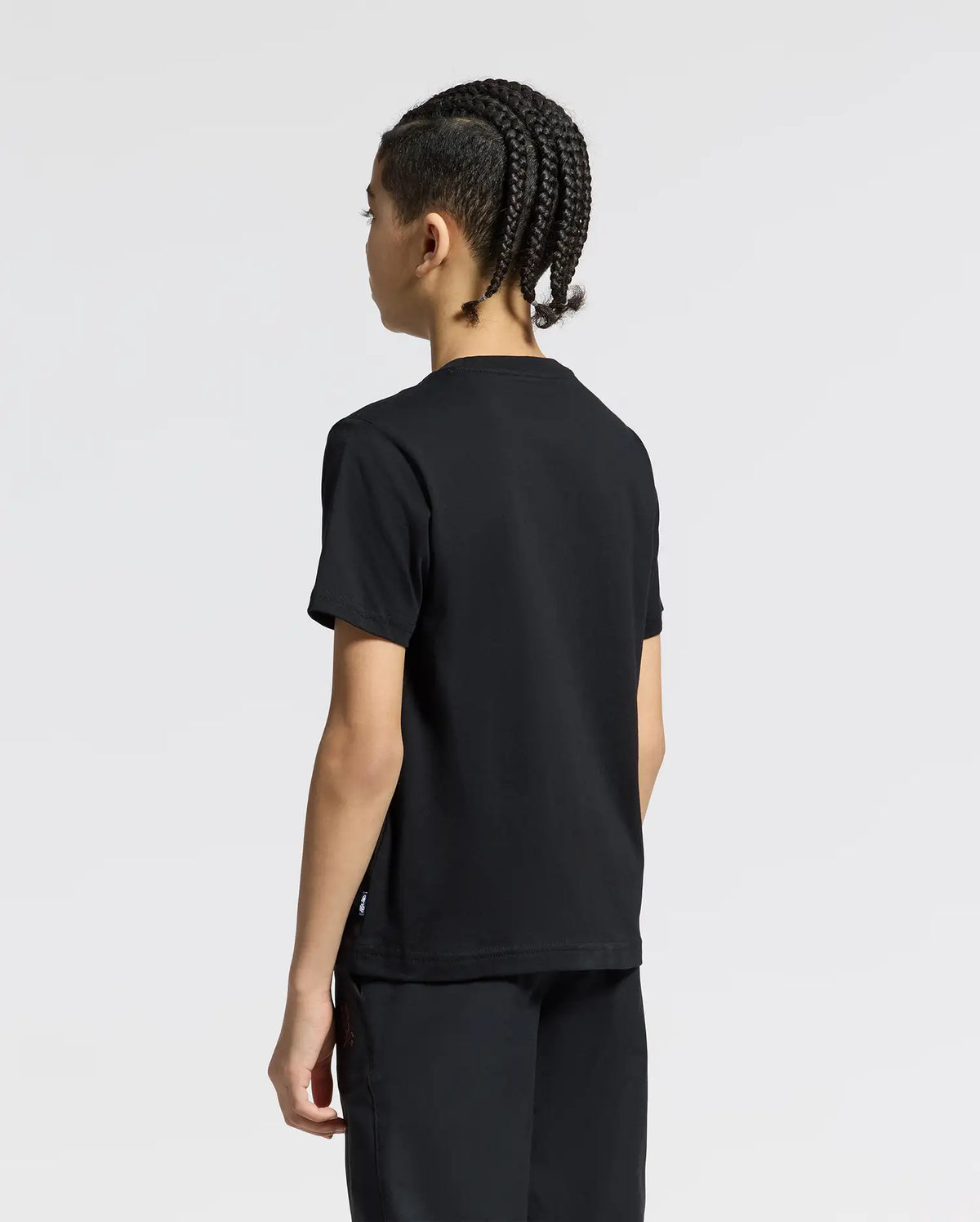 A person with braided hair is seen from the back, wearing the Psycho Bunny KIDS ANDROS GRAPHIC TEE - B0U525F200 and black pants made from 100% Pima Cotton, set against a plain white background.