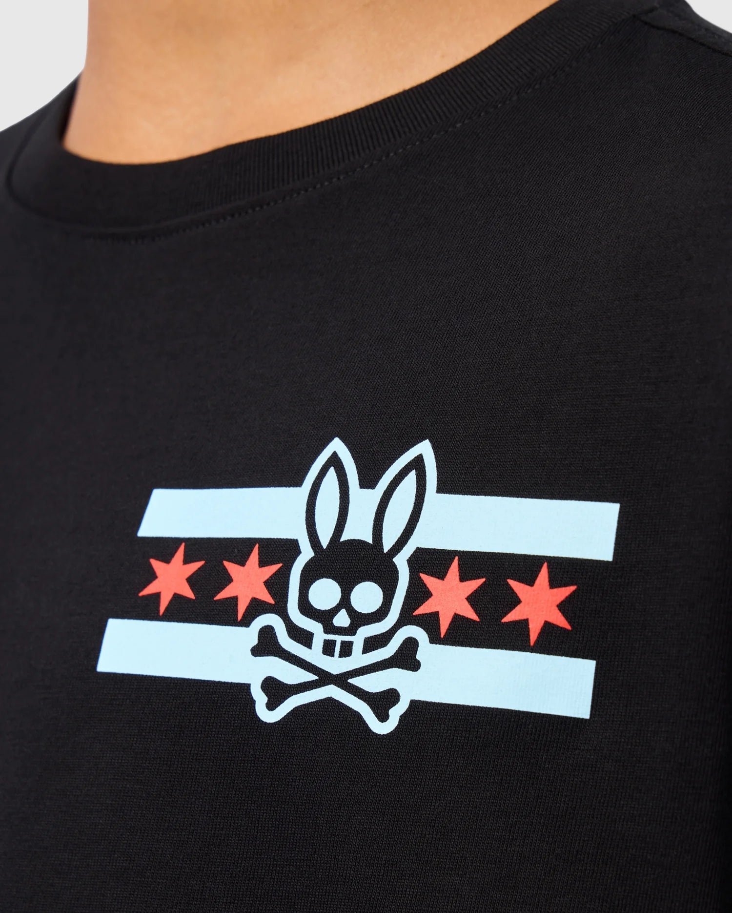 This Kids Chicago City Tee by Psycho Bunny highlights a black T-shirt adorned with a skull-and-crossbones design featuring bunny ears. It incorporates light blue stripes and four red stars reminiscent of the Chicago flag, crafted from Pima cotton jersey to ensure maximum comfort.
