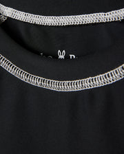 Close-up image of a black KIDS SHORT SLEEVE ANTI-UV RASHGUARD - B0U558C200 with white stitching around the neckline of the garment. The inside label is partially visible, featuring a small white outline of a rabbit head. This short sleeve rashguard offers UPF 50+ protection for ultimate sun safety from Psycho Bunny.