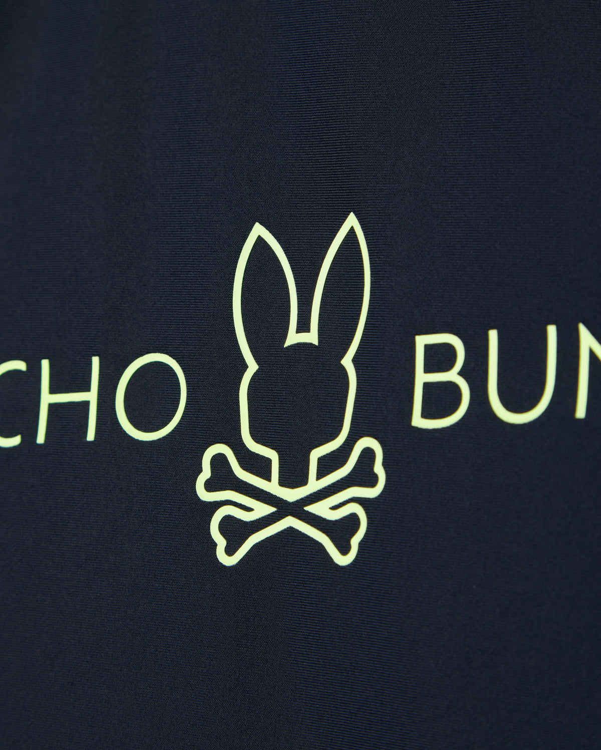 Navy blue fabric of the KIDS SHORT SLEEVE RASH GUARD - B0U558C200 by Psycho Bunny features a neon yellow bunny head above crossed bones with partial text on either side.