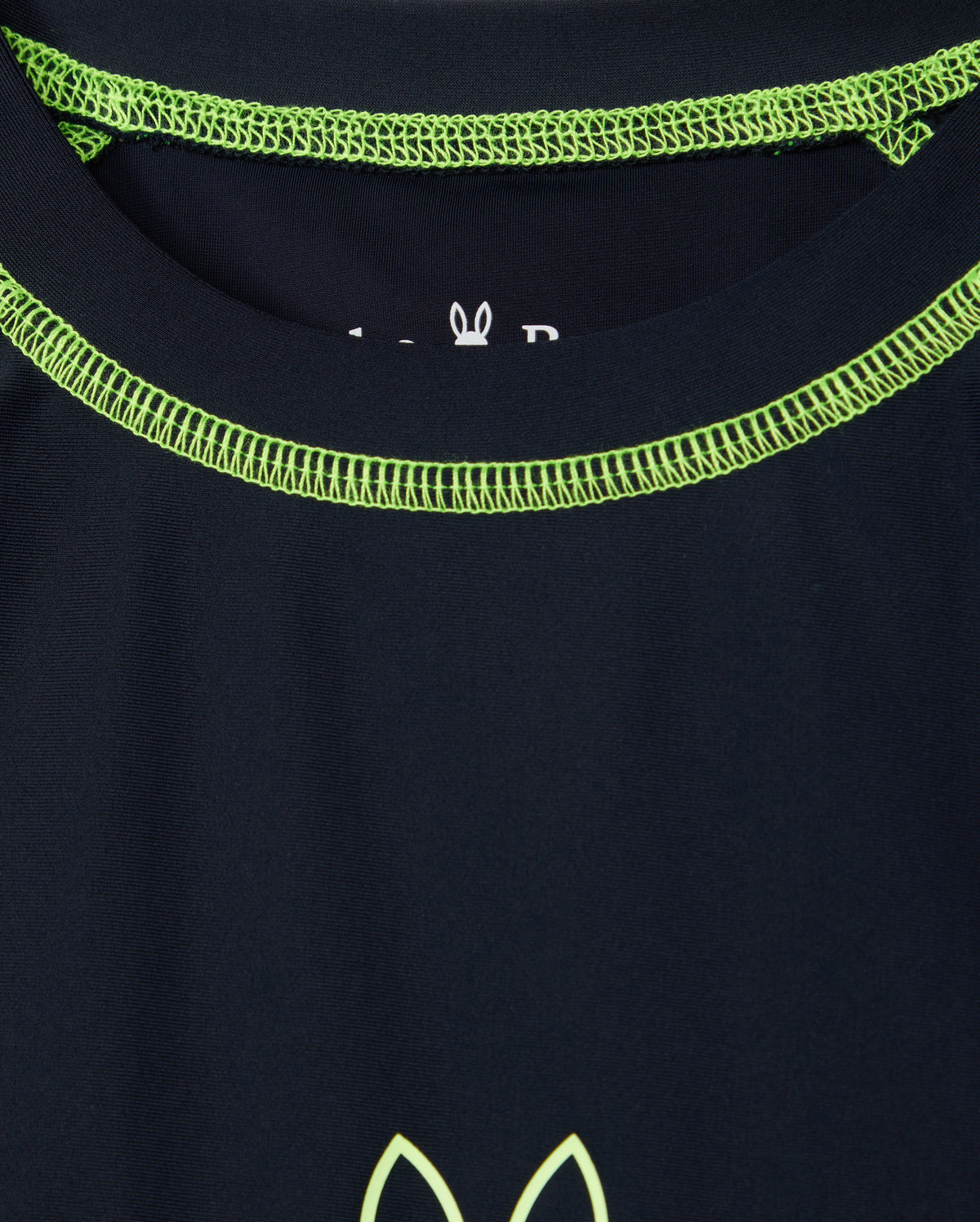 A close-up of the Psycho Bunny KIDS SHORT SLEEVE RASH GUARD in navy blue featuring lime green stitching around the neckline and a partial logo with a stylized animal design near the center.