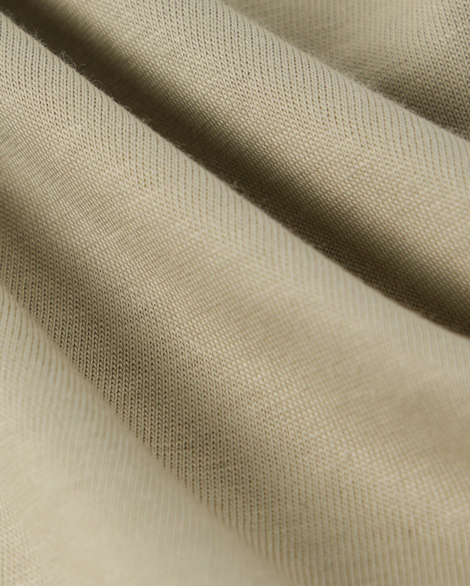 Close-up image of beige fabric with a textured, ribbed surface. The soft and slightly stretchy material, perfect for a Psycho Bunny KIDS KAYDEN FASHION TEE - B0U577C200, presents gentle folds that create depth and dimension. Made from Pima cotton, the knit pattern is smooth and even throughout.