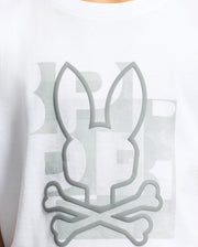Close-up of the KIDS ZEALAND GRAPHIC TEE by Psycho Bunny in soft Pima cotton, featuring a big bunny logo with crossbones below. The embossed gray design is positioned over faded background text.