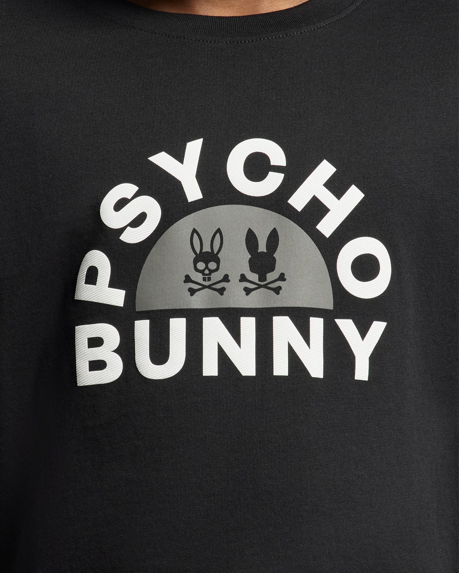 The KIDS GOLDIE GRAPHIC TEE - B0U606F200 from Psycho Bunny is a stylish black tee made of Peruvian Pima cotton, showcasing a bold white "Psycho Bunny" logo and two bunny skulls with crossbones in a semi-circle, perfect for making a statement.