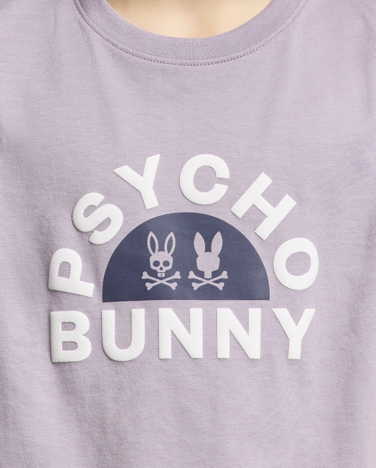 A close-up of the KIDS GOLDIE GRAPHIC TEE by Psycho Bunny, made from luxurious purple Peruvian Pima cotton, features bold white "PSYCHO BUNNY" text with unique stylized bunny graphics and crossed bones.