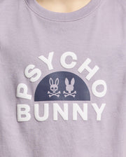 A close-up of the KIDS GOLDIE GRAPHIC TEE by Psycho Bunny, made from luxurious purple Peruvian Pima cotton, features bold white "PSYCHO BUNNY" text with unique stylized bunny graphics and crossed bones.