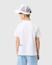 A young person from behind wearing a Psycho Bunny Kids Houston Graphic Tee and a white mesh-back cap, standing against a light gray background.