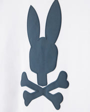 A dark grey silhouette of a stylized skull and crossbones, where the skull is replaced with a rabbit head with elongated ears, embroidered on a Psycho Bunny Pima cotton t-shirt against a plain white background.