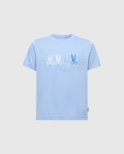 The KIDS OCEANIA EMBROIDERED GRAPHIC TEE by Psycho Bunny, product B0U607F200, features retro light blue Pima cotton with embroidered bunny skull and crossbones in varying shades. Blue bunnies are on the right and a white bunny on the left. A small label decorates the bottom left hem.