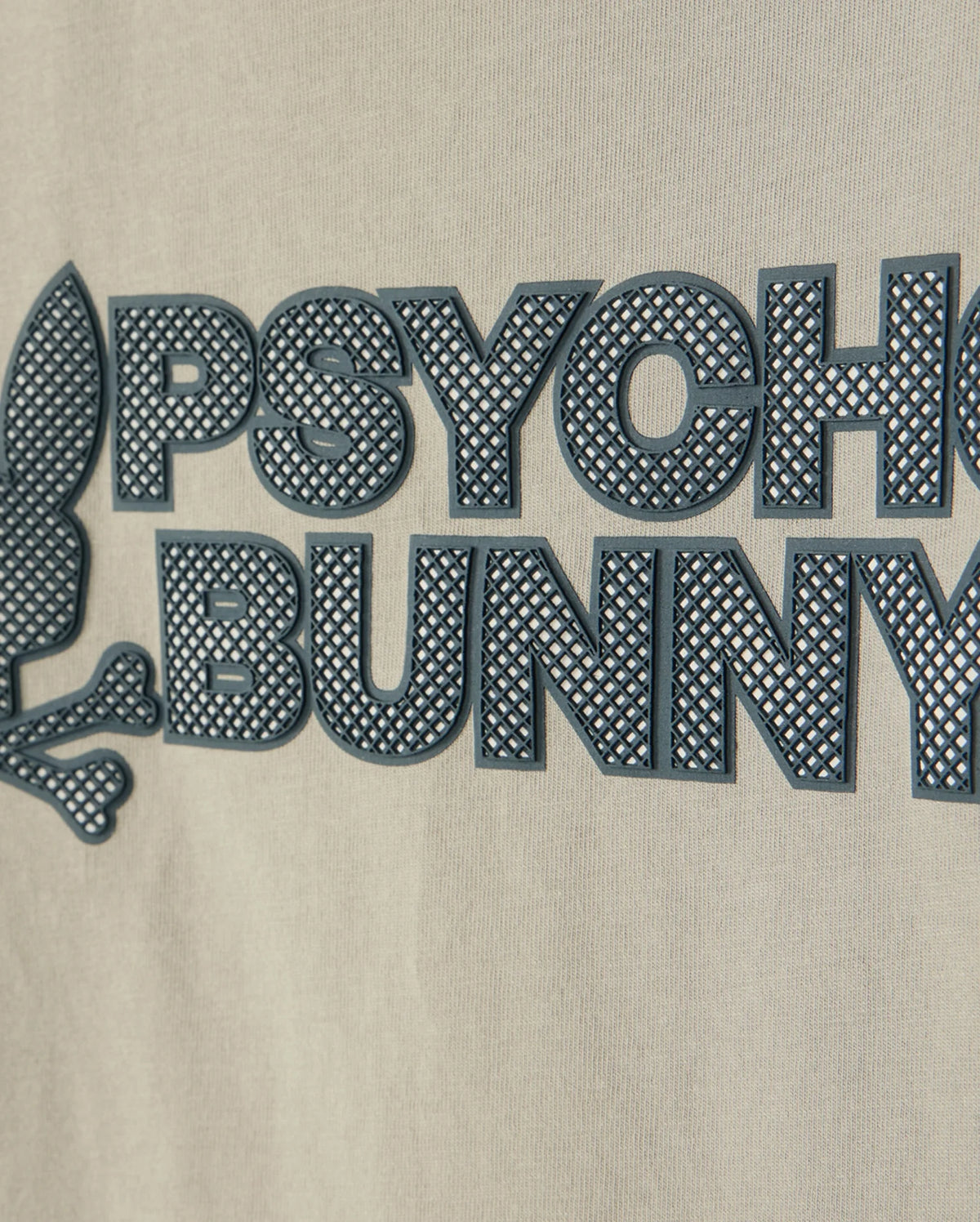 Close-up of a beige fabric with a raised graphic design showcasing an HD-silicone print. The image features the words "PSYCHO BUNNY" in black, capital letters beside a stylized rabbit head and crossbones emblem. Crafted from premium Pima cotton, this is the KIDS MELVIN GRAPHIC TEE - B0U663C200 by Psycho Bunny.