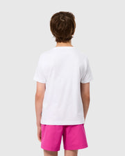 A person with short brown hair is seen from the back, wearing a KIDS MELVIN GRAPHIC TEE by Psycho Bunny and bright pink shorts. The background is a solid light gray.