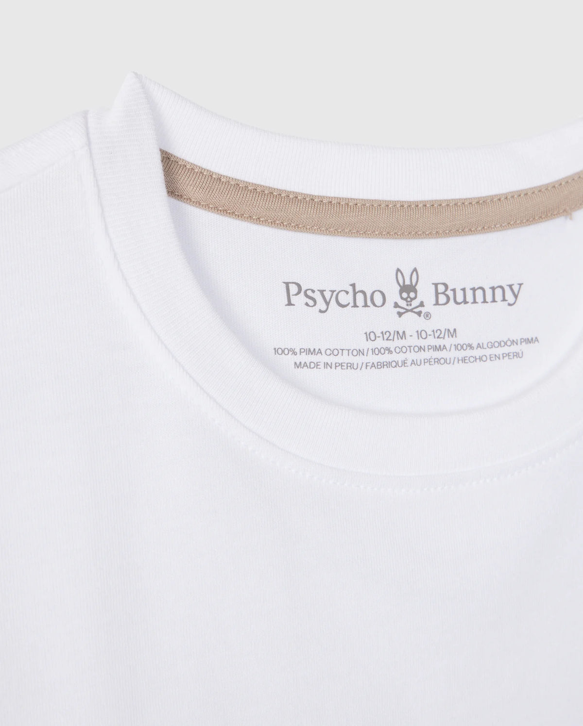 A close-up photo of a white Psycho Bunny KIDS MELVIN GRAPHIC TEE - B0U663C200. The image focuses on the collar area, showing brand details and size information, with a Bunny with wordmark printed on the inner neck label. The shirt is made of 100% Pima cotton and it is made in Peru.