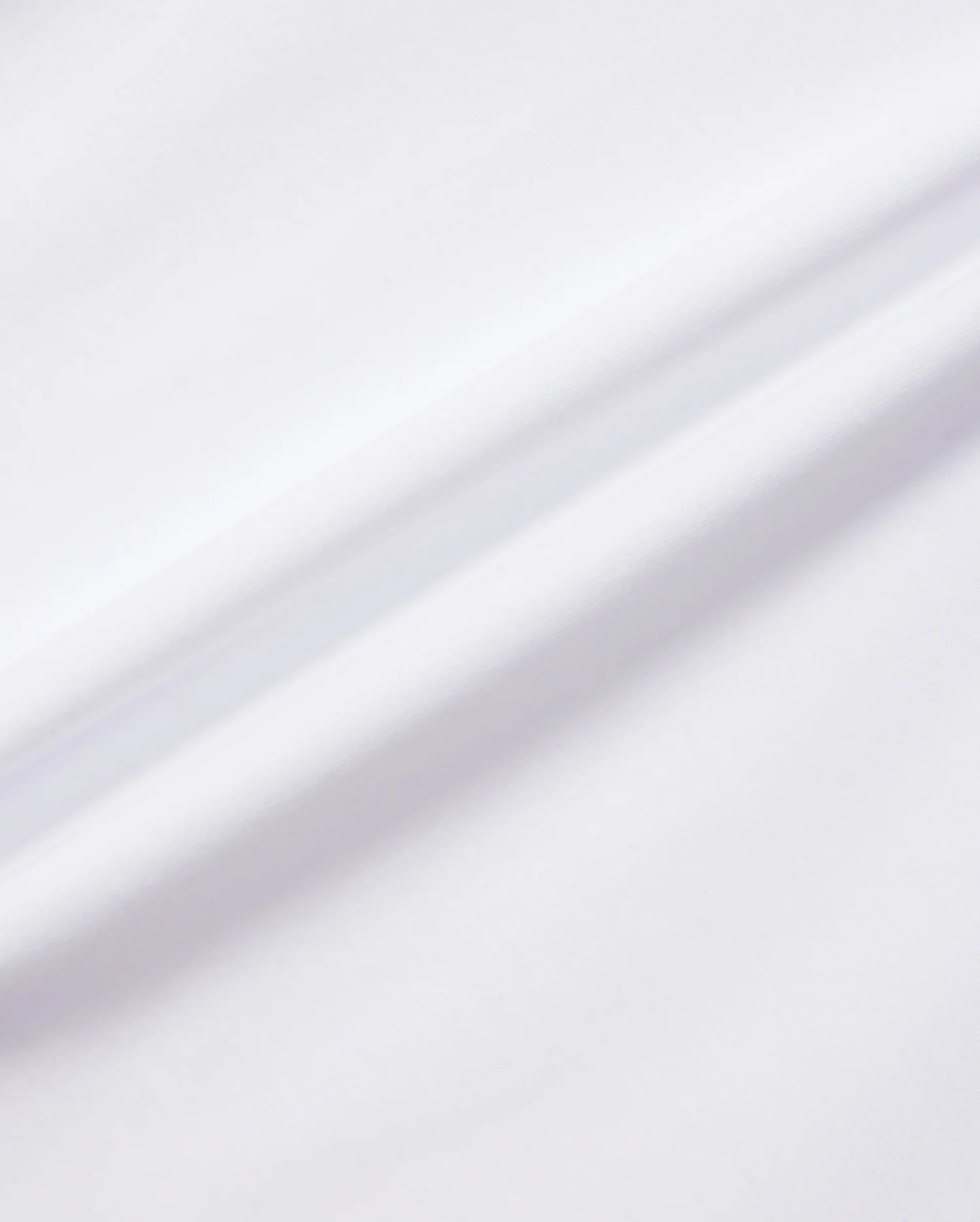 A close-up shot of the white KIDS MELVIN GRAPHIC TEE - B0U663C200 from Psycho Bunny showcases the Pima cotton fabric's soft, smooth texture, with a subtle diagonal crease running through the middle. The lighting accentuates the fabric’s clean and minimalist appearance, making it perfect for graphic applications.
