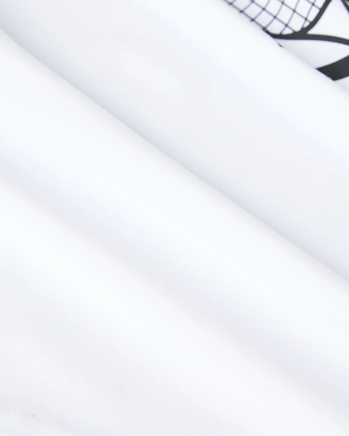 Close-up of smooth, white fabric with a subtle fold and a part of a black geometric pattern visible at the top right corner. The texture appears soft and slightly reflective under the lighting, reminiscent of a high-quality performance-led jersey, much like the Psycho Bunny KIDS COURTSIDE GRAPHIC TEE - B0U681C200.