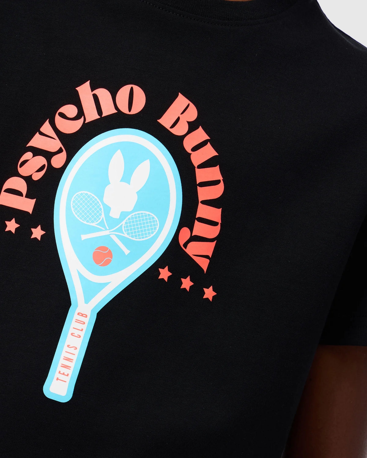 Close-up of the KIDS COURTSIDE GRAPHIC TEE - B0U682C200 from Psycho Bunny, featuring a black background with a blue tennis racket, two racquets, an orange tennis ball, and a signature white bunny logo. The words "Psycho Bunny" are elegantly arched above in pink letters, accompanied by six small pink stars for a vibrant tennis-inspired design.