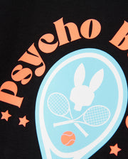 A close-up of a black fabric showcases the text "psycho b" in orange, arranged in an arc. At the center, there's a light blue emblem with a silhouette of a bunny's head above two crossed tennis rackets and a tennis ball. This performance-focused jersey by Psycho Bunny is bordered with orange stars, making the KIDS COURTSIDE GRAPHIC TEE - B0U682C200 perfect for kids' tennis-inspired adventures.
