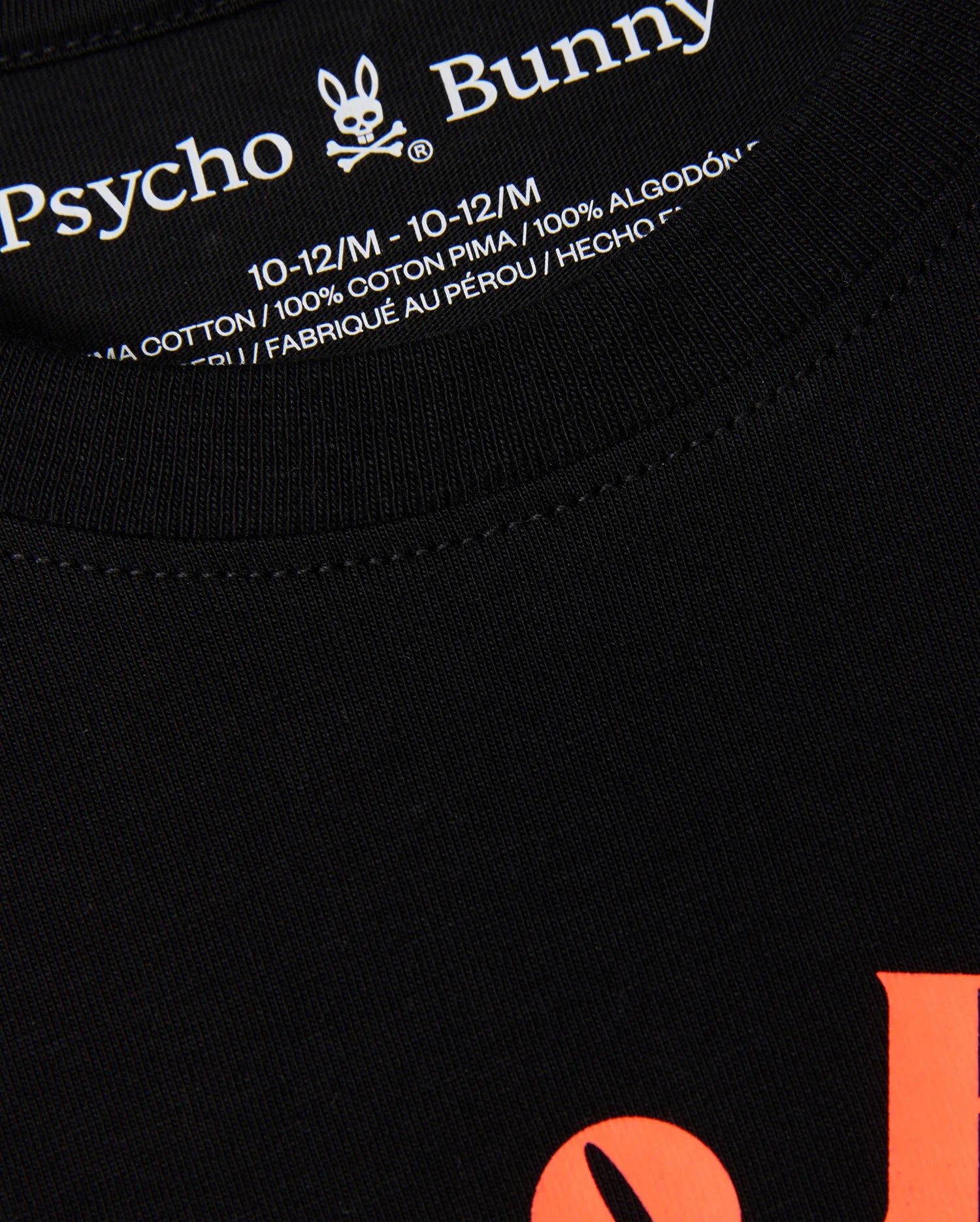Close-up of the label on a black KIDS COURTSIDE GRAPHIC TEE - B0U682C200 by Psycho Bunny, showing size 10-12/M in white text. This kids' graphic tee boasts orange lettering on the front and is crafted from 100% pima cotton. Made in Peru, this tennis-inspired piece combines style and comfort.