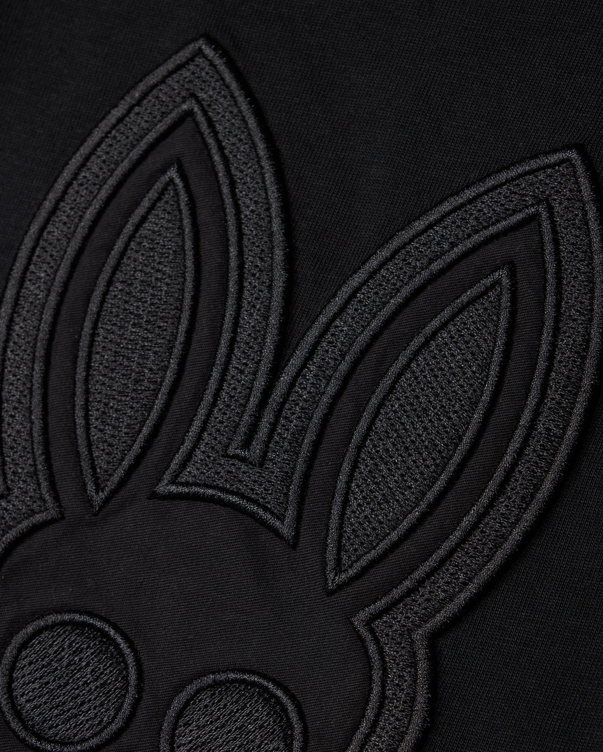 Close-up of a black fabric featuring an embroidered outline of a cartoon rabbit's face and ears, designed in a minimalist style with a monochromatic black-on-black color scheme. Showcasing Peruvian craftsmanship, the KIDS MALTON GRAPHIC TEE - B0U795D200 by Psycho Bunny is made from luxurious Pima cotton, adding texture and contrast.