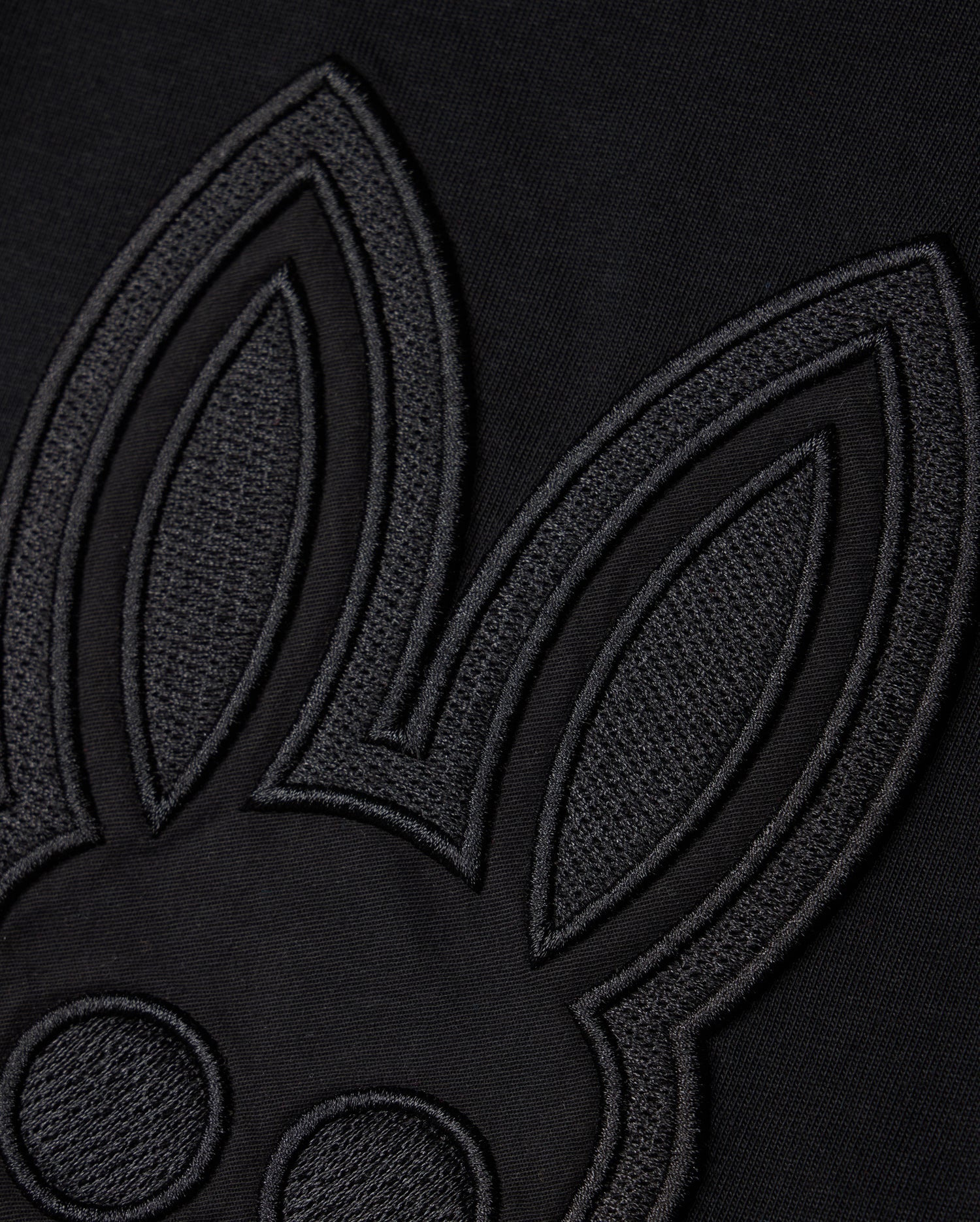 Close-up of a black fabric featuring an embroidered outline of a cartoon rabbit's face and ears, designed in a minimalist style with a monochromatic black-on-black color scheme. Showcasing Peruvian craftsmanship, the KIDS MALTON GRAPHIC TEE - B0U795D200 by Psycho Bunny is made from luxurious Pima cotton, adding texture and contrast.