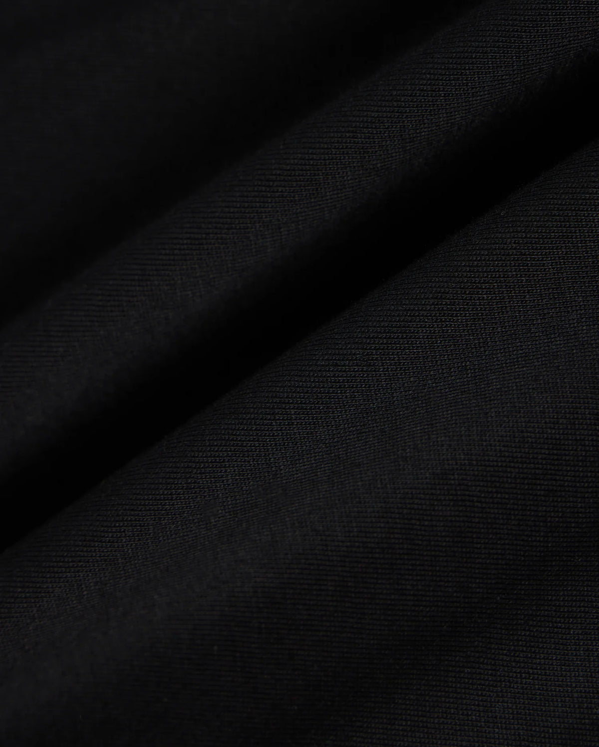 Close-up view of the fabric of the KIDS MALTON GRAPHIC TEE - B0U795D200 by Psycho Bunny, featuring a black hue with a smooth texture and visible fine weave, showcasing subtle diagonal folds and ripples, reminiscent of Peruvian craftsmanship.